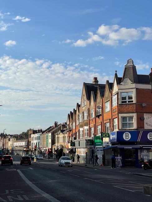 This image shows a street scene in Deptford during daytime, with a row of multi-story residential buildings featuring brick and painted facades, some with bay windows and decorative gables. The street