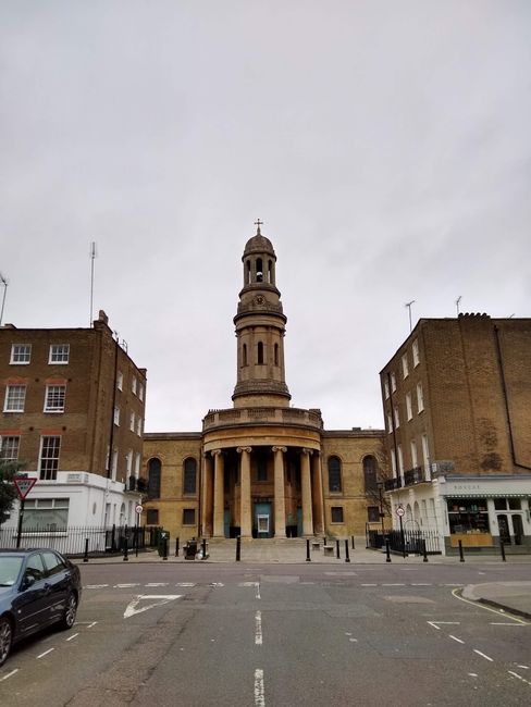 A street scene in Deptford with a row of multi-storey terraced residential buildings featuring brick facades, some with decorative window frames and chimneys, under a cloudy sky. On the pavement, ther